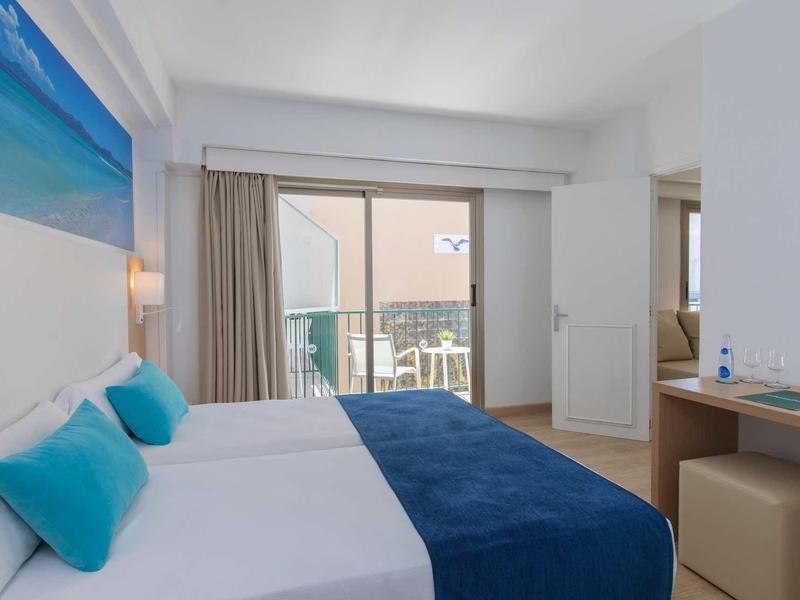 Bright hotel room with double bed, blue pillows, and balcony