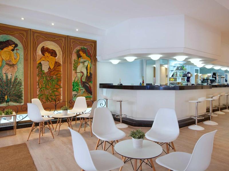 Modern lounge area with white chairs, glass tables, and decorative wall art in a bright room.