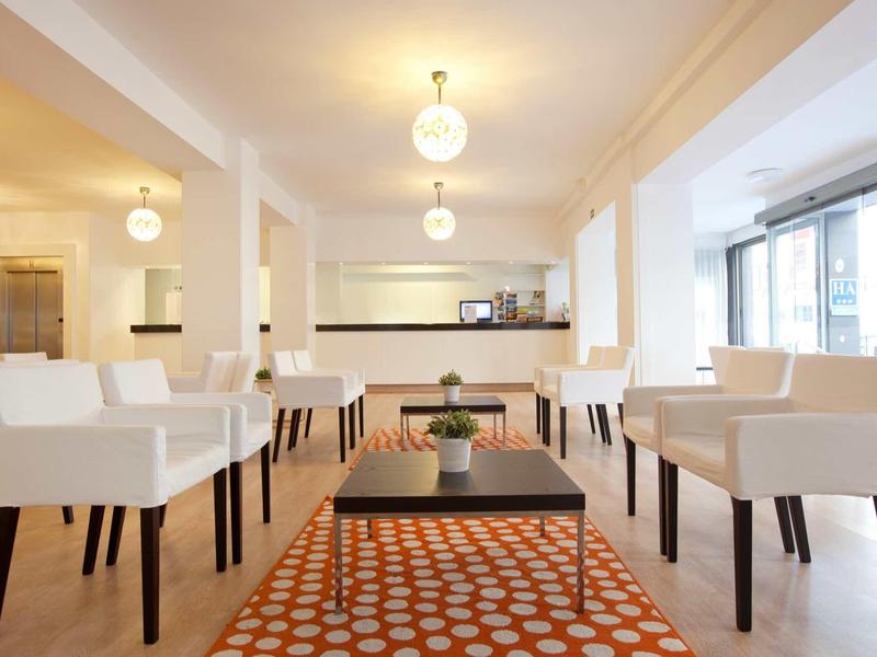 Bright modern hotel lounge area with white armchairs and an orange patterned carpet.