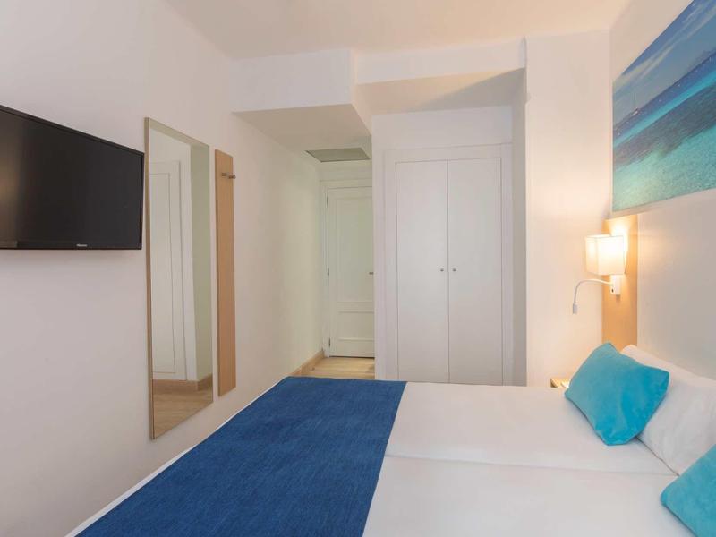 Bright hotel room with double bed, blue accents, and wall mirror.