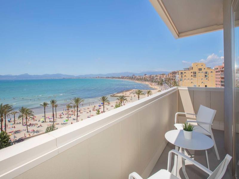 Balcony with table and chairs overlooking beach, palm trees, and sea on a sunny day.