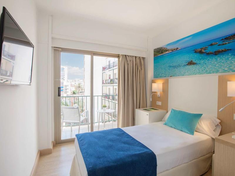 Bright hotel room with single bed, blue blanket, and sea view artwork on the wall.