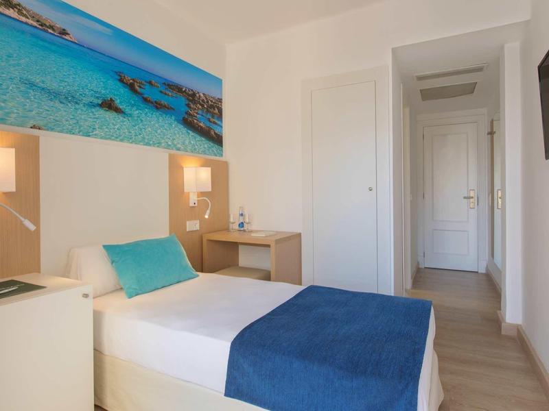 Single room with white bedding, blue throw, and coastal picture on the wall.