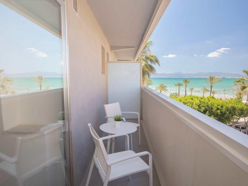 Balcony with two white chairs and small table overlooking palm trees and sea.
