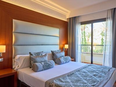 Gemütliches Hotelzimmer mit großem Bett und Balkon mit Blick auf Bäume.