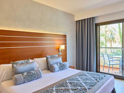 Modernes Hotelzimmer mit Doppelbett, dekorativen Kissen und Zugang zu einem Balkon mit Gartenblick.