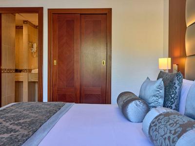 Modernes Hotelzimmer mit breitem Bett, dekorativen Kissen und Holztüren im Hintergrund.