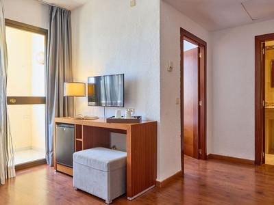 Heller Hotelzimmerflur mit Holzboden, TV, Schreibtisch und Hocker neben einem Balkon