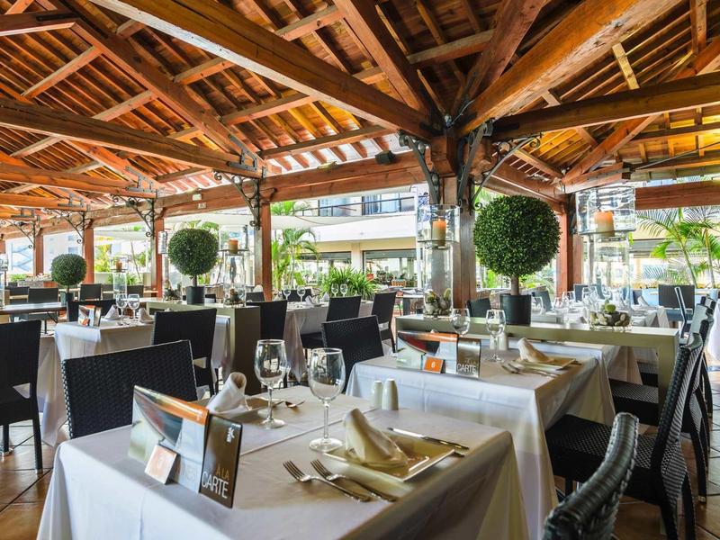 Ristorante dell'hotel con tavoli apparecchiati bianchi, sedie nere e soffitto in legno.