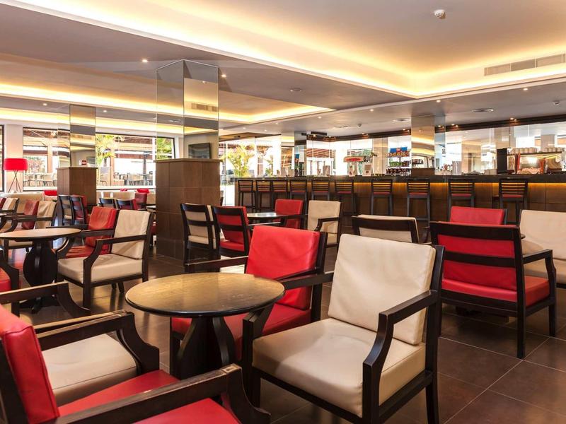 Area bar dell'hotel moderna con comode sedie rosse e bianche e tavoli rotondi in legno.