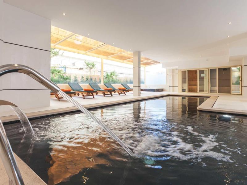 Piscina interna con lettini e grandi finestre che lasciano entrare la luce del giorno.