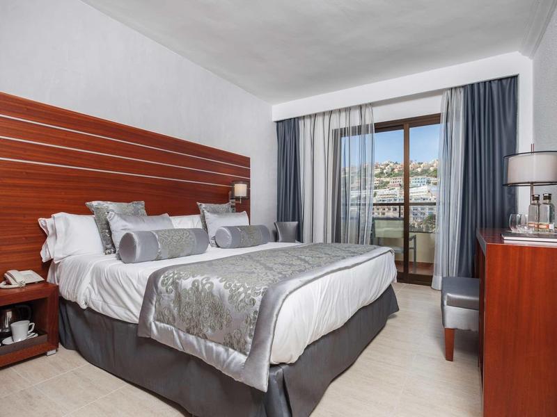 Camera d'albergo luminosa con letto matrimoniale, parete con accento in legno e balcone con vista.