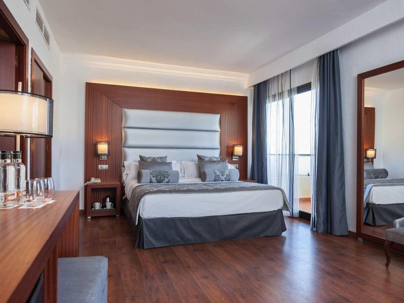 Camera d'hotel moderna con letto matrimoniale, mobili in legno e grande finestra con tende.