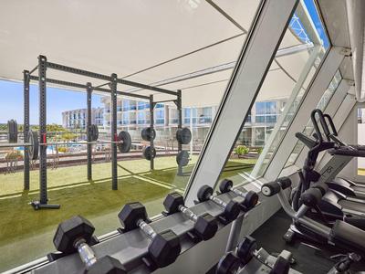 Fitnessruimte met halterrek, loopbanden en grote ramen met uitzicht op buitenruimte.