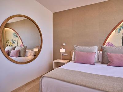 Moderne slaapkamer met grote ronde spiegel en roze accentkussens op het bed.