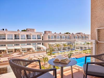 Uitzicht op een hotelzwembad met ligstoelen vanaf een balkon met twee stoelen en een tafel met een boek.