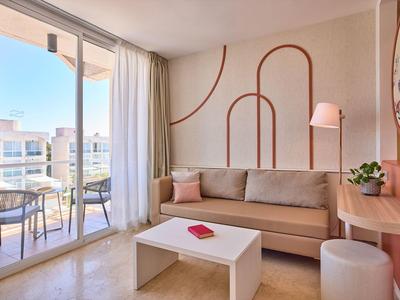 Modern ingerichte hotelkamer met bank, tafel en balkon met zitgedeelte.