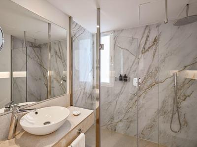 Moderne badkamer met marmeren muren, wastafel en inloopdouche met regendouchekop.