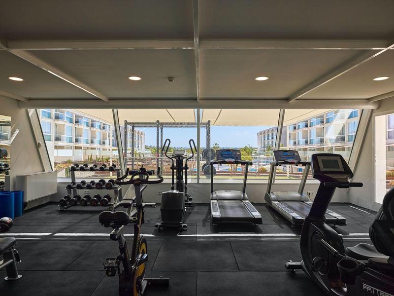 Modern fitnesscentrum met loopbanden, halters en uitzicht op het hotelzwembad.