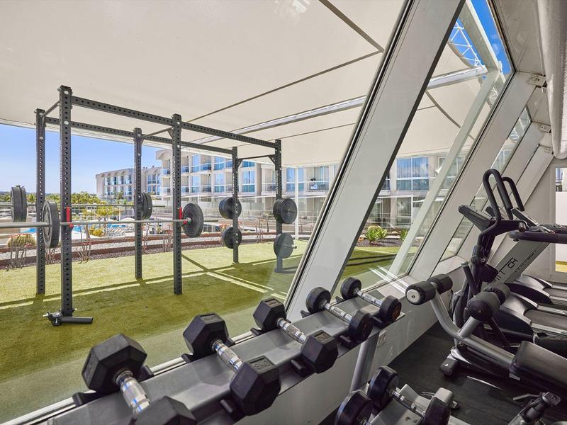 Fitnessruimte met halters, loopbanden en uitzicht op een buitenruimte met fitnessapparatuur.