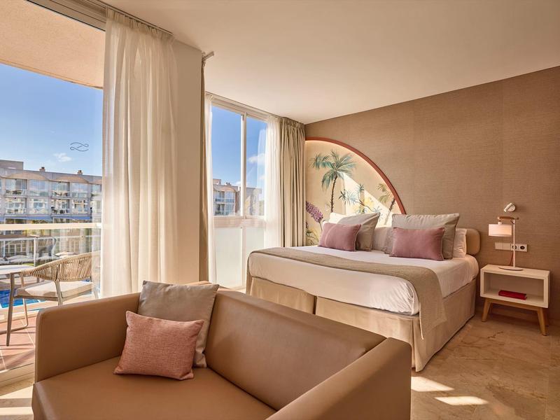 Lichte hotelkamer met groot raam, tweepersoonsbed, bank en balkon met uitzicht op de stad.