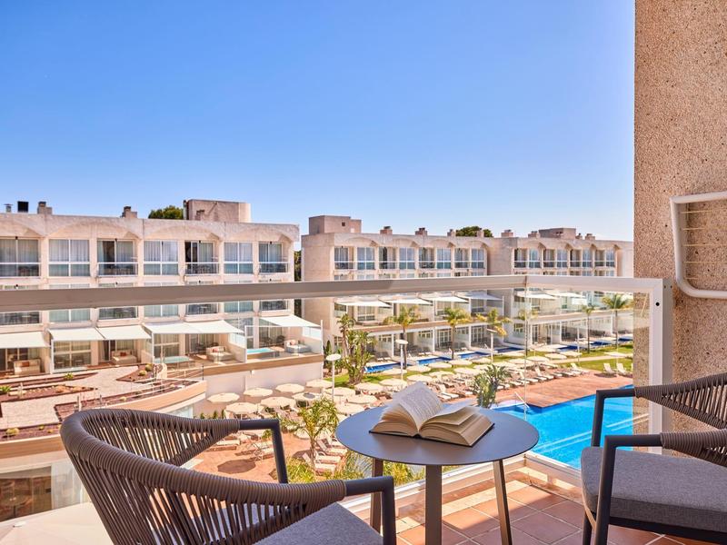 Uitzicht op een hotelzwembad met ligstoelen vanaf een balkon met twee stoelen en een tafel met een boek.