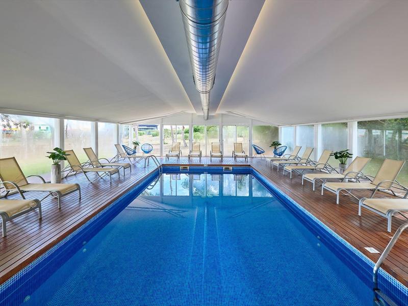 Overdekt zwembad met houten vloer en ligstoelen aan beide zijden