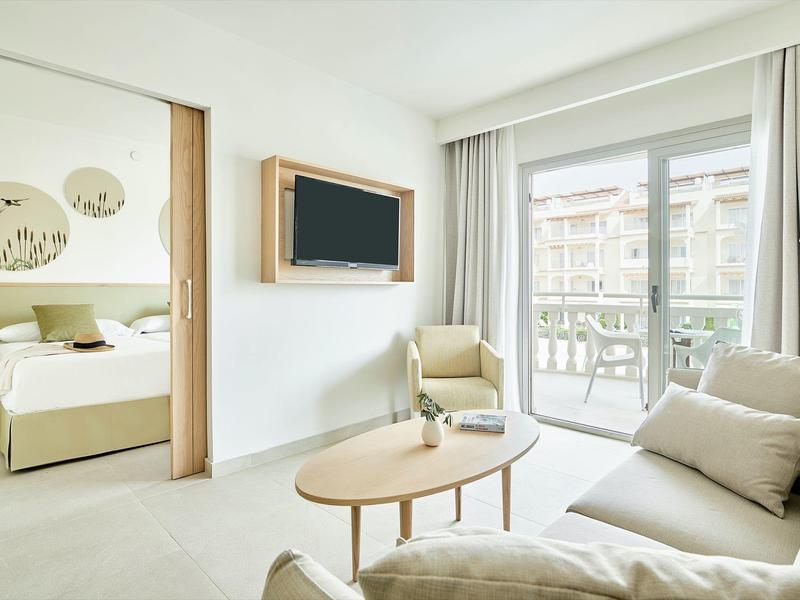 Jasny pokój hotelowy z częścią wypoczynkową, balkonem i nowoczesnym wystrojem w neutralnych kolorach.