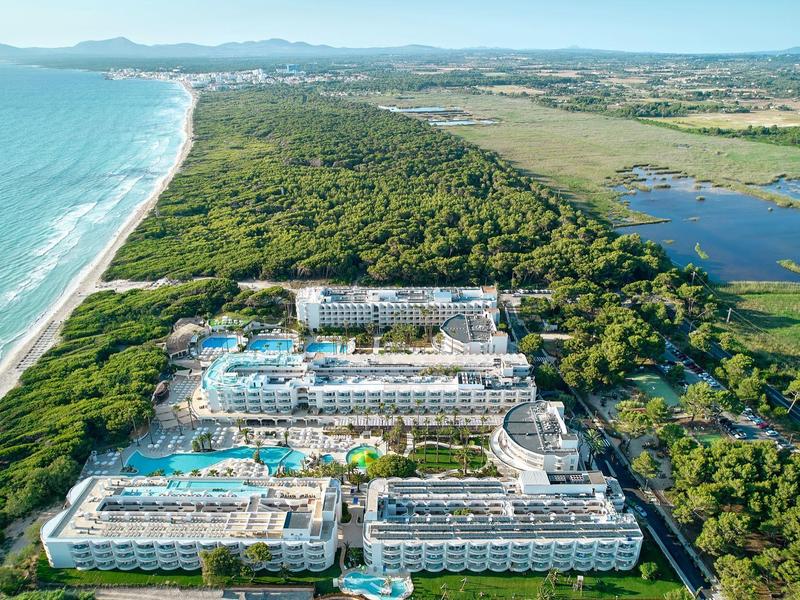 Luksusowy hotel z dużymi basenami przy długiej piaszczystej plaży i bujną roślinnością nad morzem.