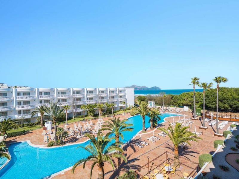 Ośrodek hotelowy z basenem, palmami i białym budynkiem pod jasnym niebieskim niebem