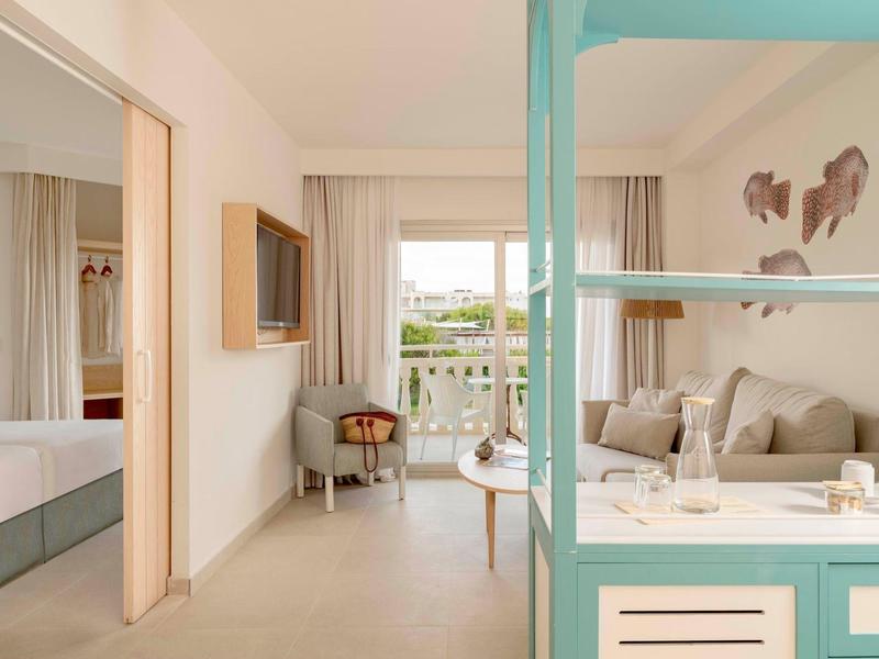 Jasny pokój hotelowy z balkonem, wygodną sofą i nowoczesnym wnętrzem.