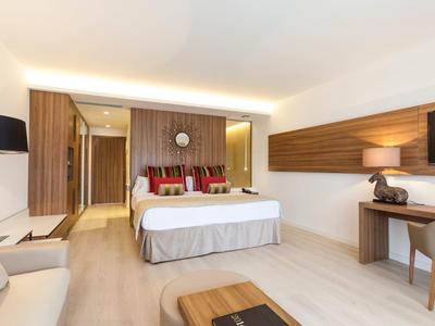 Modernes Hotelzimmer mit großem Bett, Schreibtisch, Sofa und warmweißer Beleuchtung.