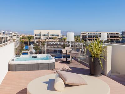 Dachterrasse mit Jacuzzi, Lounge-Möbeln, Pflanzen und klarem blauem Himmel im Hintergrund.