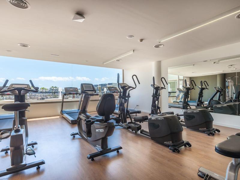 Bright gym with exercise bikes and treadmills in front of large windows with a view.