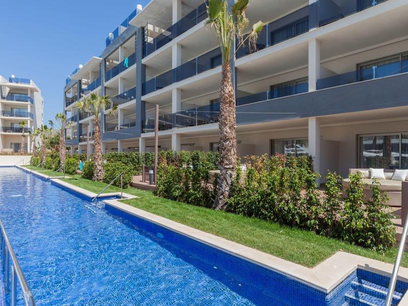 Modern residential complex with pool, palm trees, and seating areas, ideal for vacation stays.