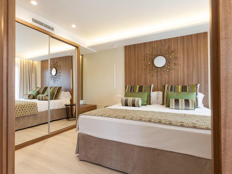 Modern hotel room with large bed, wood paneling, mirrored wardrobe, and decorative pillows.