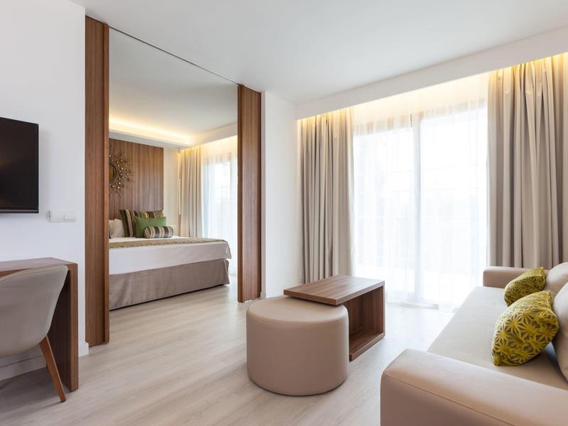 Modernly furnished hotel room with sofa, bed, desk, and large window with curtains.