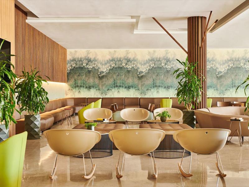 Modern hotel restaurant with comfortable chairs, green plants, and elegant wall decor.