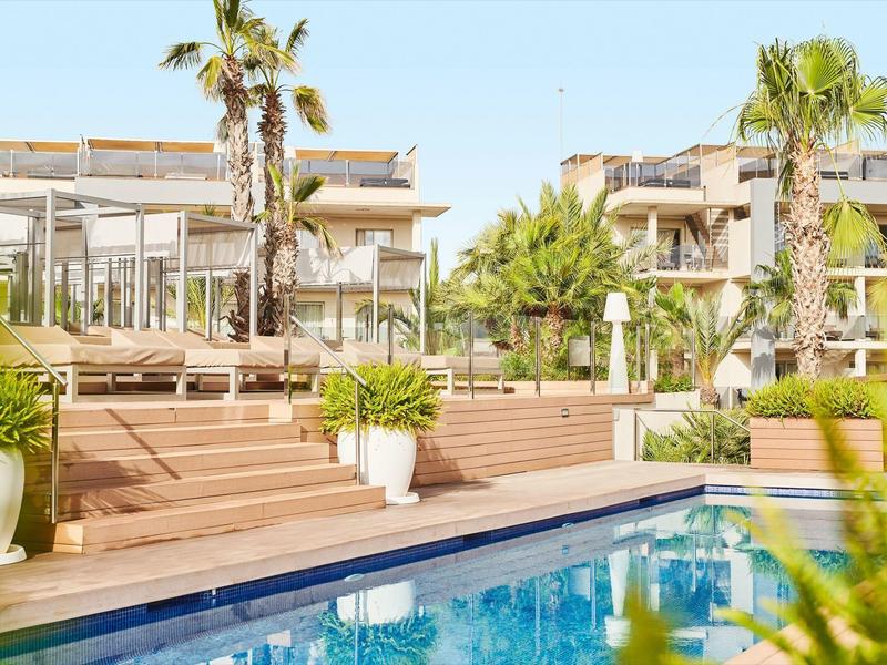 Modern outdoor pool with terrace and palm trees in front of a hotel building.