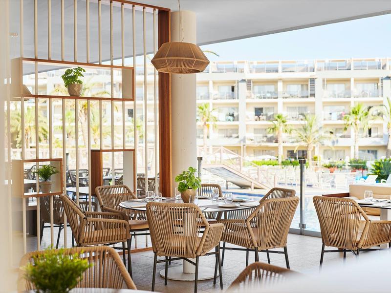 Brightly furnished hotel outdoor area with wicker chairs and large glass windows.