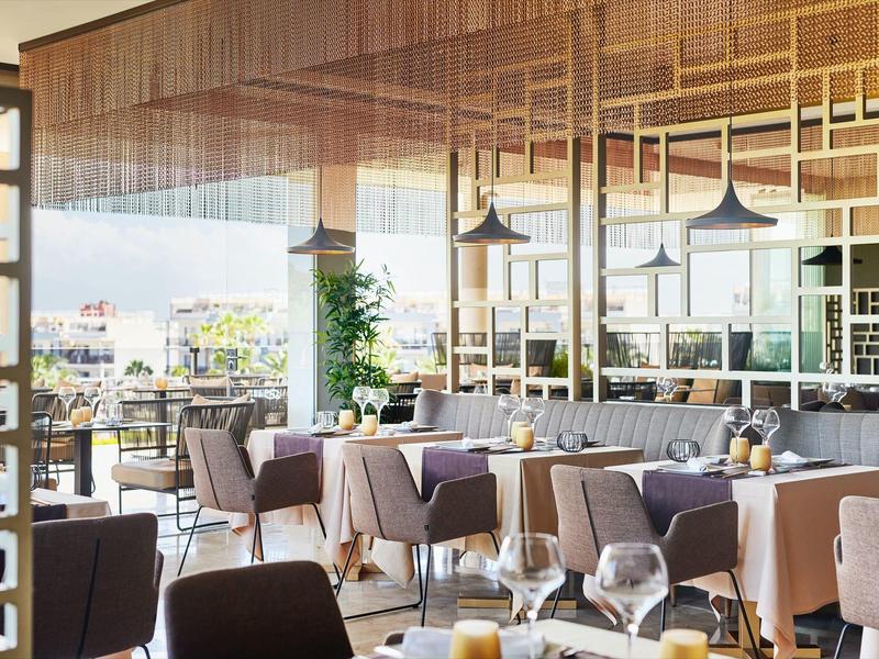 Modern restaurant with large windows, wooden elements, and elegantly set tables.