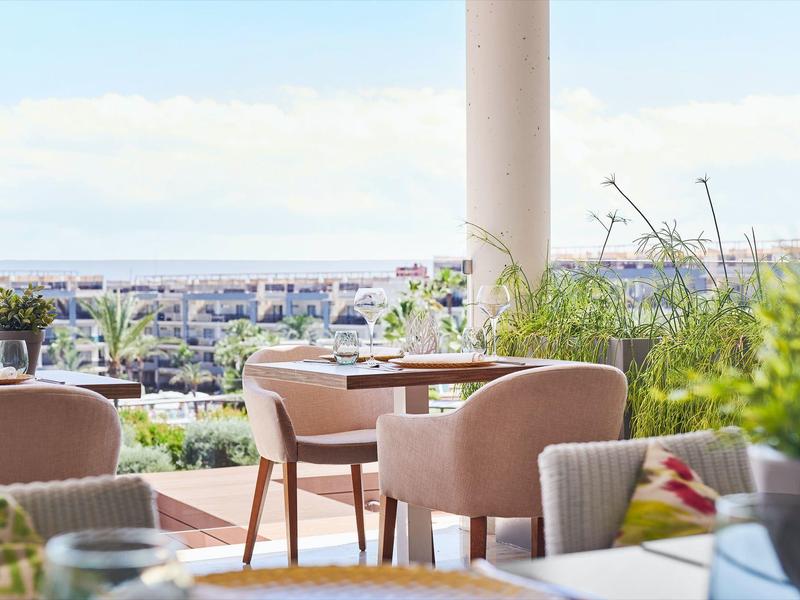 Modern hotel outdoor area with tables and chairs overlooking the city and sea.