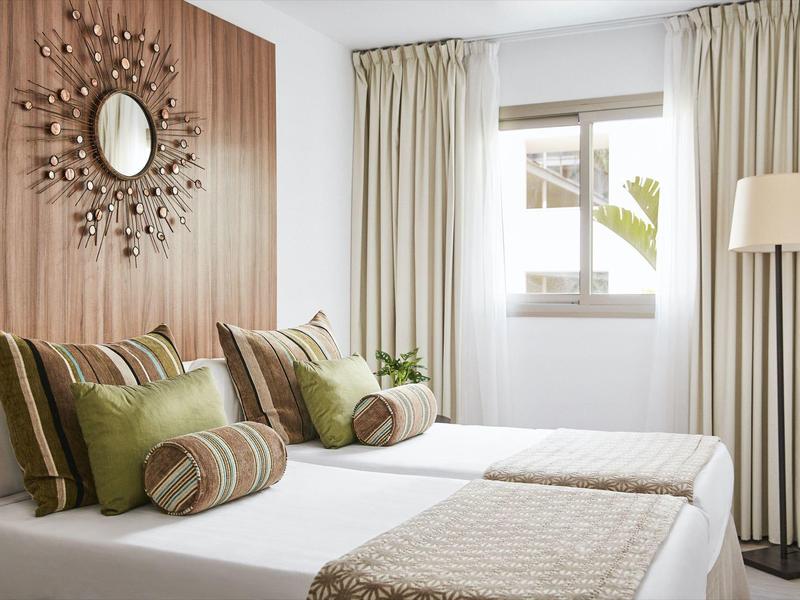 Bright hotel room with two single beds, decorative pillows, and curtains on the window.
