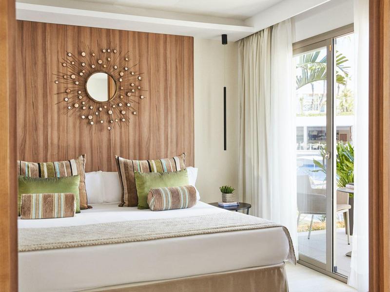 Bright hotel room with double bed, wood accents, and balcony overlooking outdoors.
