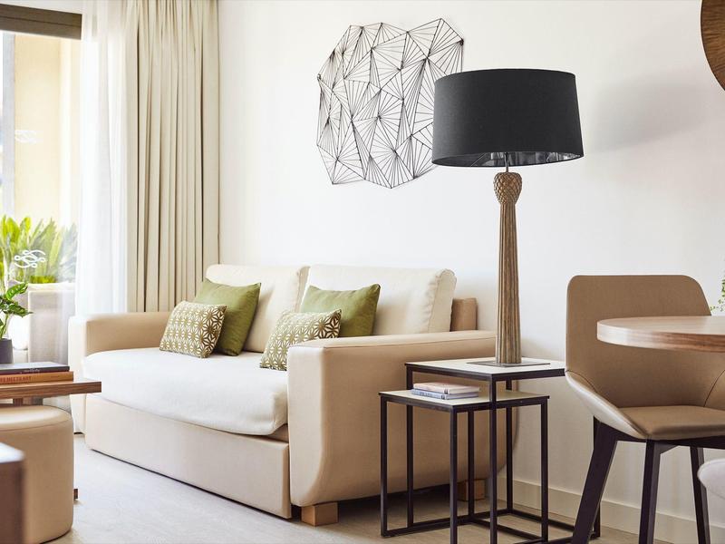 Bright living room with beige sofa, wooden lamp stand, and small table beside the sofa.
