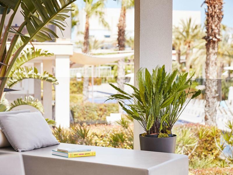 Modern outdoor area with white sofa, potted plant, and view of palm trees.