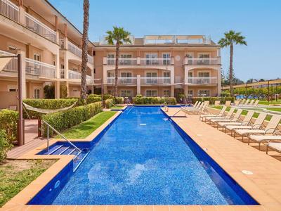 Modern outdoor pool with lounge chairs and palm trees in front of a hotel building under clear sky.
