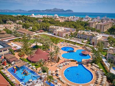 Aerial view of a large hotel pool with sun umbrellas and surrounding buildings by the sea.