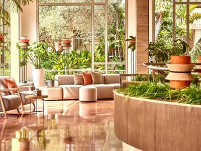 Bright hotel lobby area with plants, armchairs, and large windows