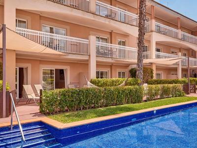 Vista exterior de un hotel con habitaciones con balcón y una piscina azul en primer plano.